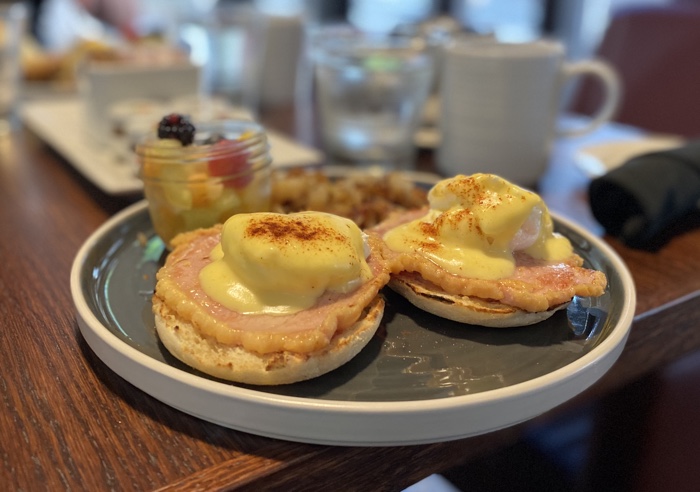 chelsea hotel eggs benedict - Ottawa Road Trips eggs benedict on a round grey-and-white plate with hash browns and a glass jar of fruit salad