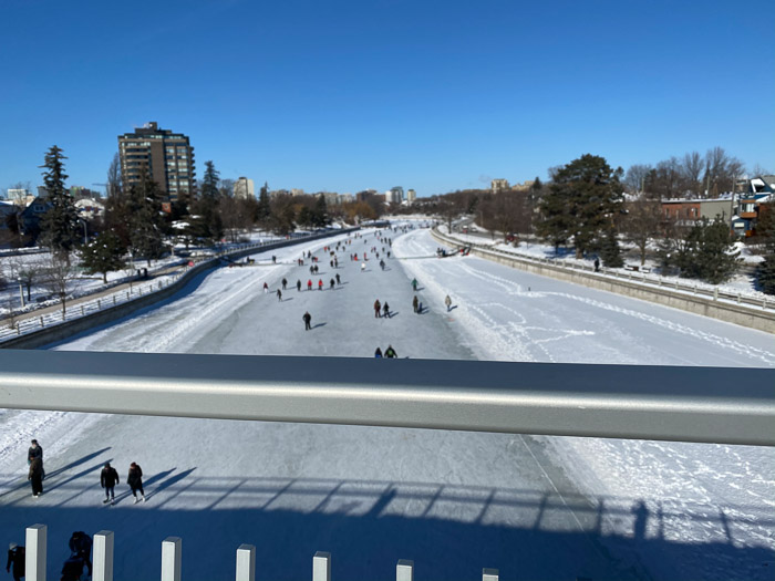 skaters on the rideau canal below a metal bridge railing