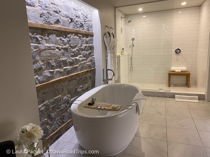 frontenac club limestone bathroom wall - Ottawa Road Trips oval soaker tub beside an exposed limestone wall, with tiled shower in background