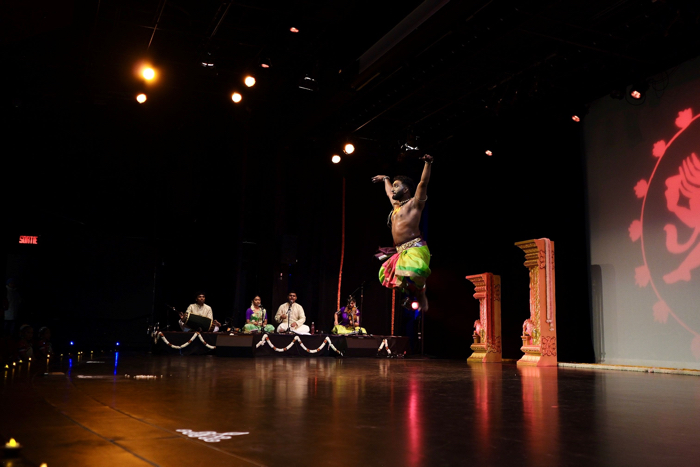 male dancer leaping in air with indian musicians in background