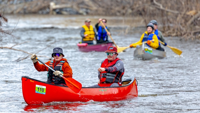 two paddlers ini a red canoe on a river, with two other canoes in background