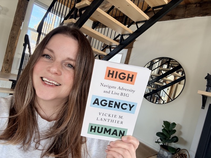 smiling woman holding up a copy of book titled high agency human