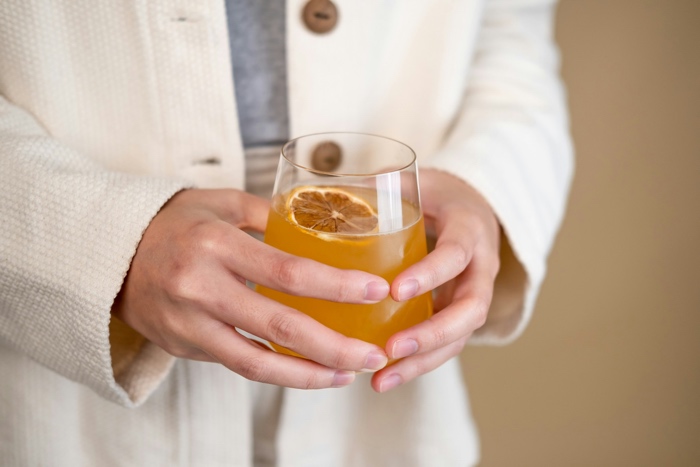 closeup of hands holding a glass of kombucha with an orange slice in it