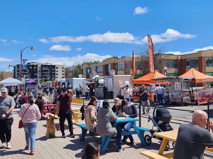 people eating outdoors at picnic tables with poutine trucks in background
