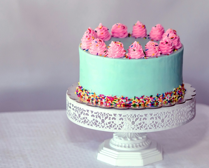 mint green cake with pink icing flowers and multi coloured sprinkles on a cake stand