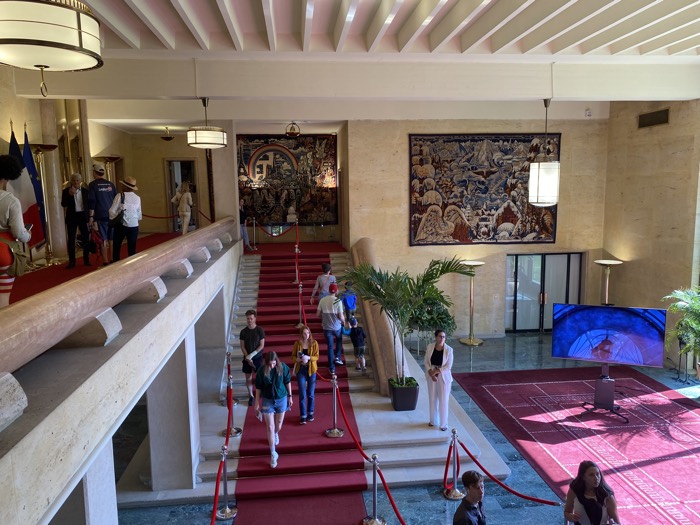 large foyer with coffered ceiling, tapestries, and marble floors, staircase and mezzanine railings