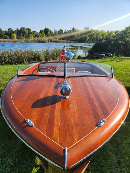 wooden speedboat on a lawn, with river in background