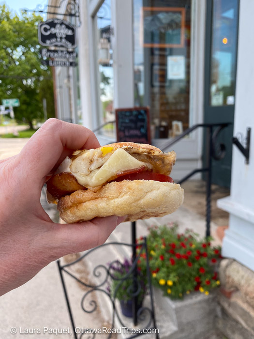 breakfast sandwich on an english muffin outside, with "coffee" sign in background