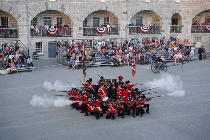 fh_sunsetceremony_aug22_2025_0036_h 700 - Ottawa Road Trips military personnel in scarlet uniforms shooting muskets outward from a circular formation.