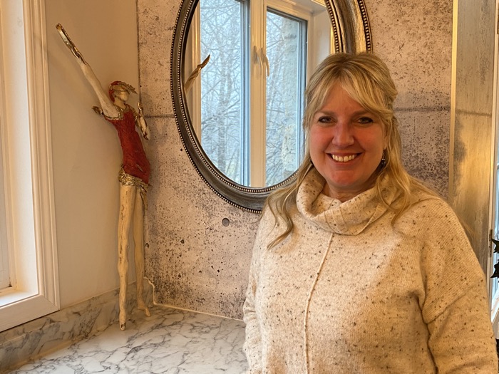 smiling blonde woman standing in front of a mirror and a sculpture