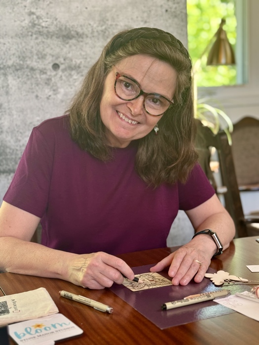 woman in purple t-shirt smiling as she uses a pencil to make a piece of art