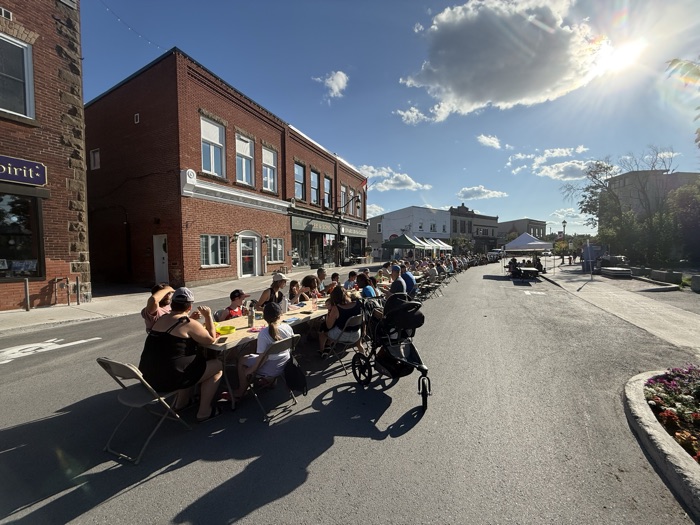 very long table down the middle of a road lined with people eating dinner