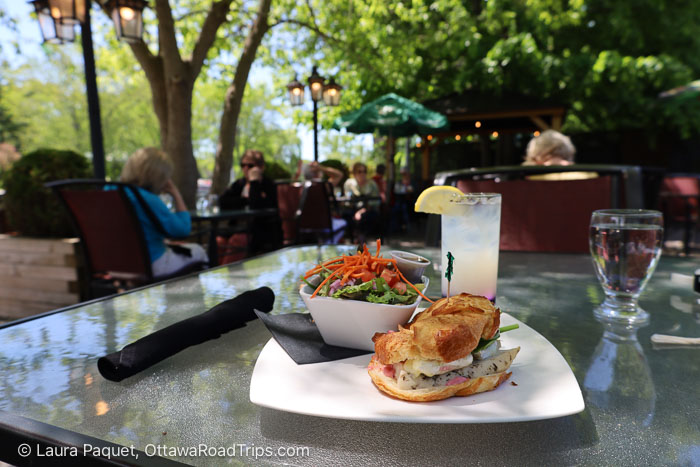 turkey sandwich on a croissant with salad and a glass of lemonade on a glass table on an outdoor patio