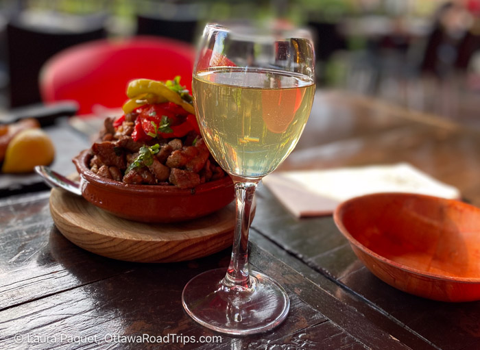 glass of white wine and a bowl of carnitas on a wooden table