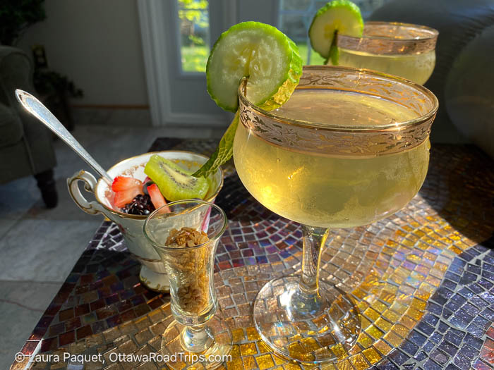 two margarita glasses with lime wedges on a colorful mosaic table, a fruit dessert cup and a granola shooter beside them.