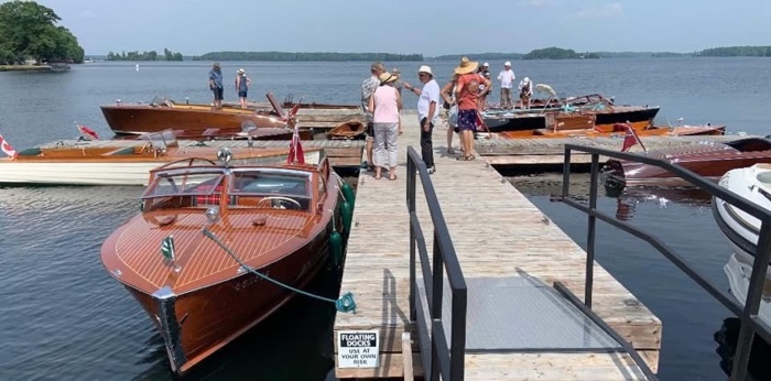 people looking at antique wooden boats moored at a wooden dock in portland ontario
