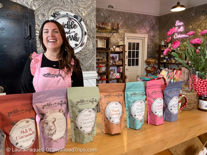 laughing woman in a pink apron behind bags of caramels on a wooden counter