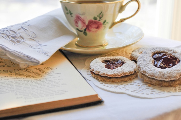 haley-parson-tea-cookies-unsplash - Ottawa Road Trips china cup and saucer, linen napkin, jam cookies on a doily, and a book