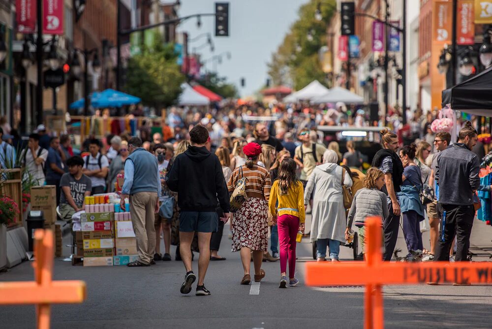 crowds of people walking past vendor booths on a street closed to traffic