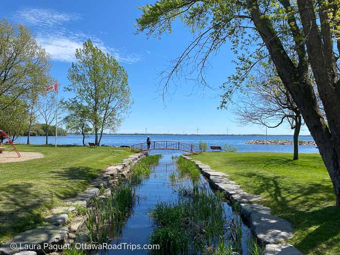 person standing on a bridge across a creek where it runs into lake ontario