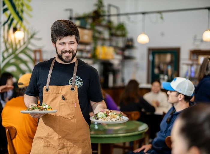 man in apron bringing plates of food to tables at otter creek kitchen in kingston.