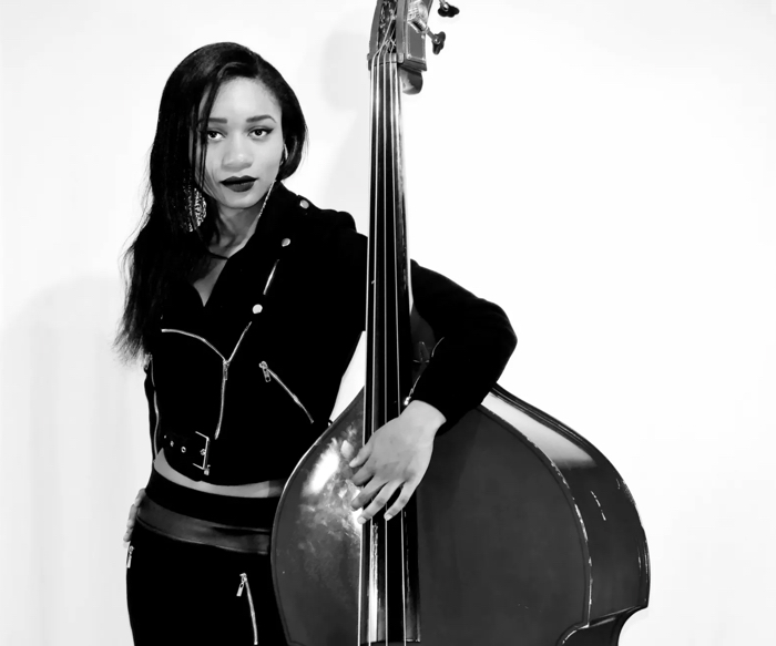 angelique francis - Ottawa Road Trips female musician posing with an upright bass in a black jacket, looking at the camera against a white background.